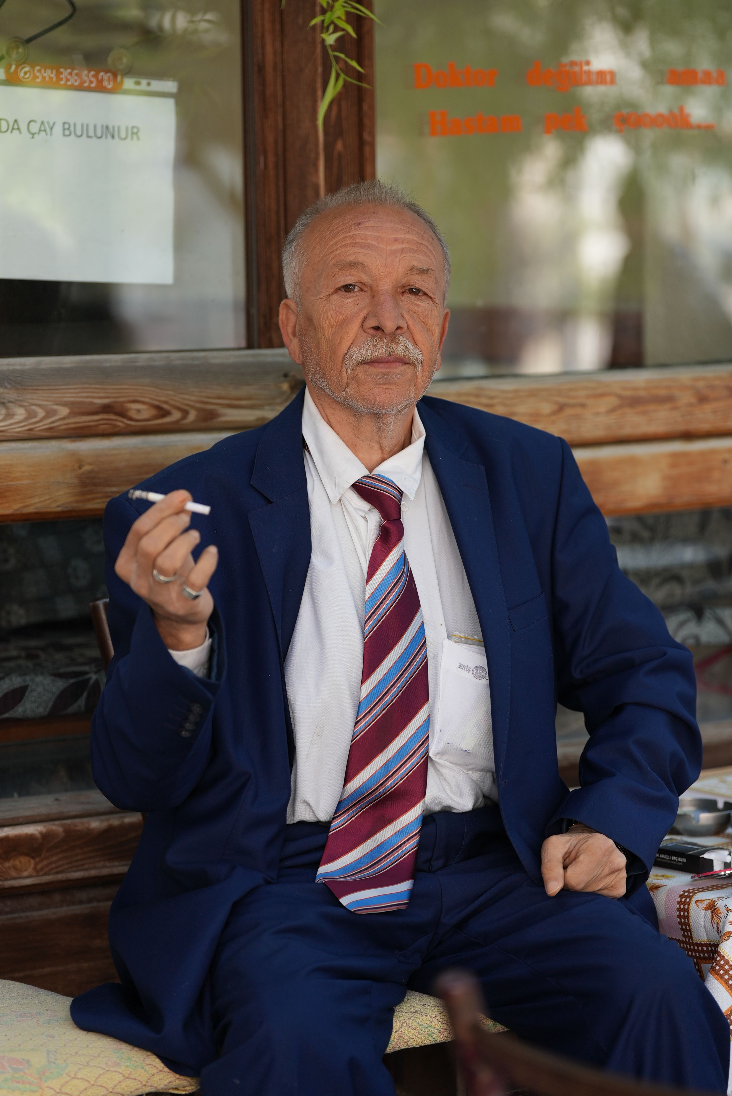 Elderly man in blue suit sitting outdoors smoking, capturing a moment of relaxation.