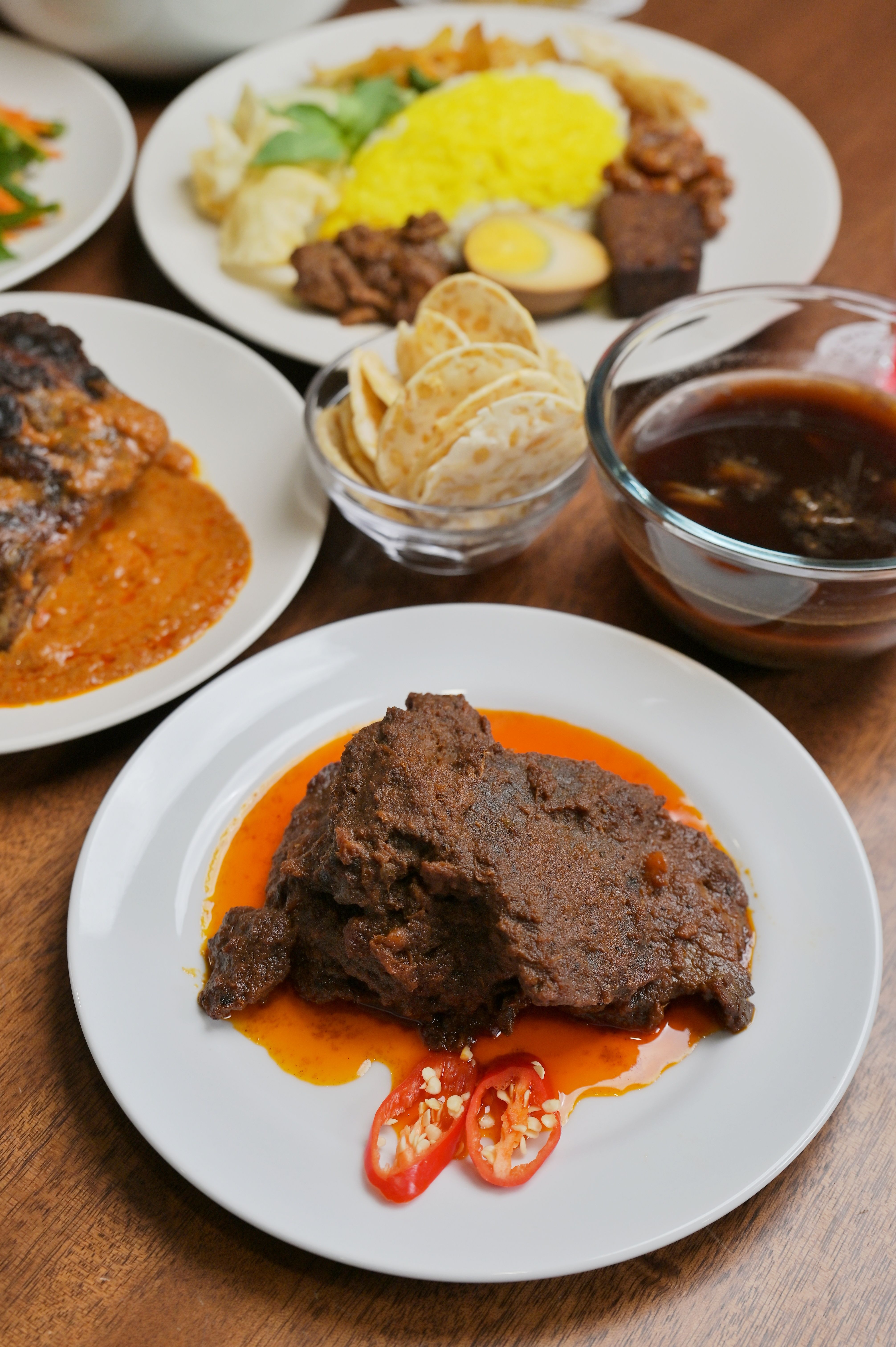 A serving of rendang daging showing tender beef cubes coated in glossy brown-rust chilli-coconut sauce, with a metal spoon resting in the bowl.