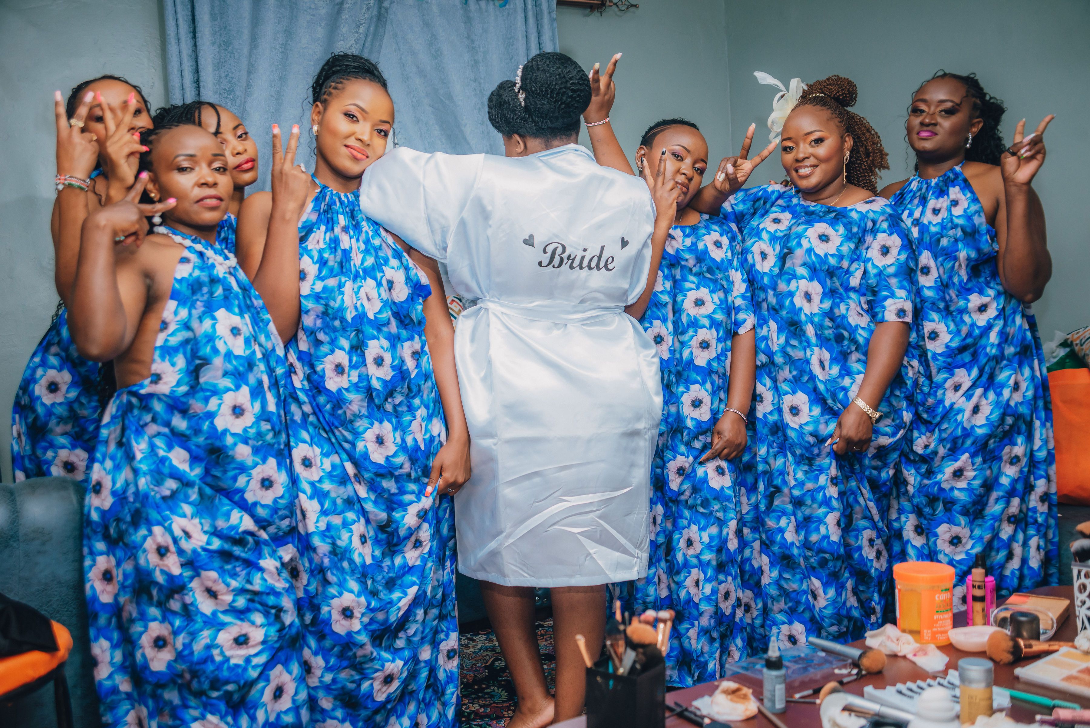 A joyful Kenyan bride with bridesmaids in blue floral dresses, celebrating indoors.