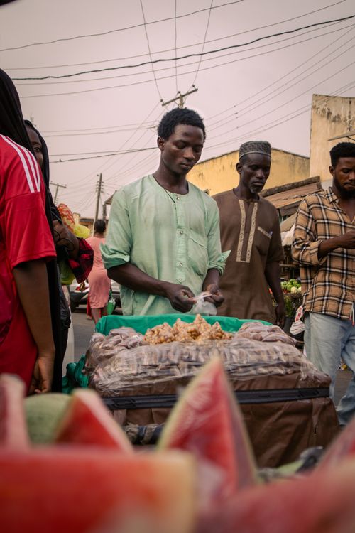 Free A street vendor surrounded by customers in a bustling African market setting with fresh produce. Stock Photo