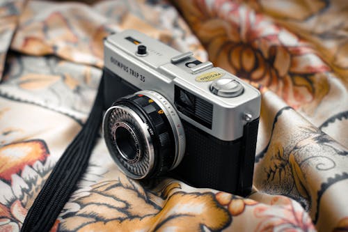 Closeup of shiny vintage photo camera placed on smooth textile in retro flat