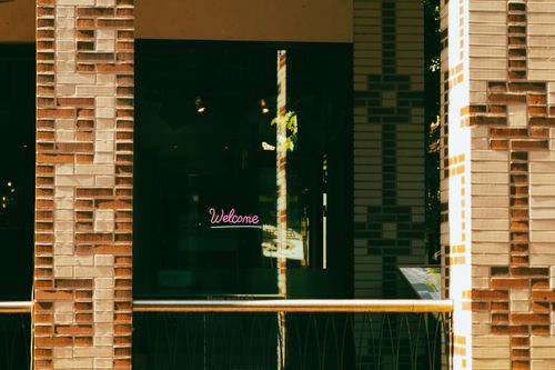 Free Stylish neon 'Welcome' sign on an urban brick facade with a modern aesthetic. Stock Photo