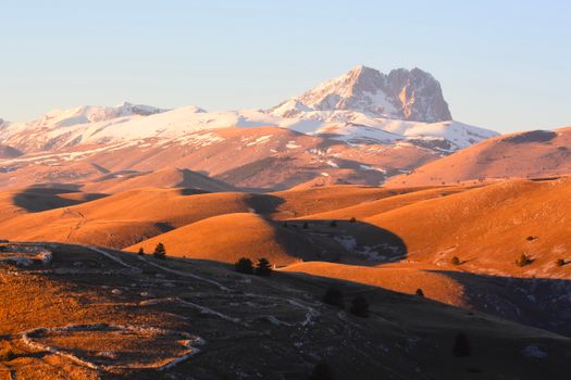 Warm sunset light over the snow-capped Gran Sasso mountains in Calascio, Abruzzo, Italy.