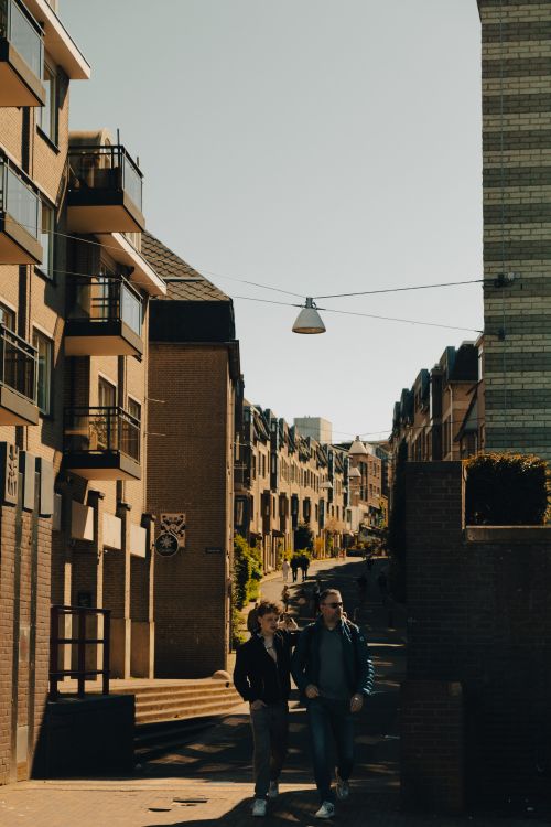 Free Two people walking along a city street during day, surrounded by apartment buildings under clear skies. Stock Photo