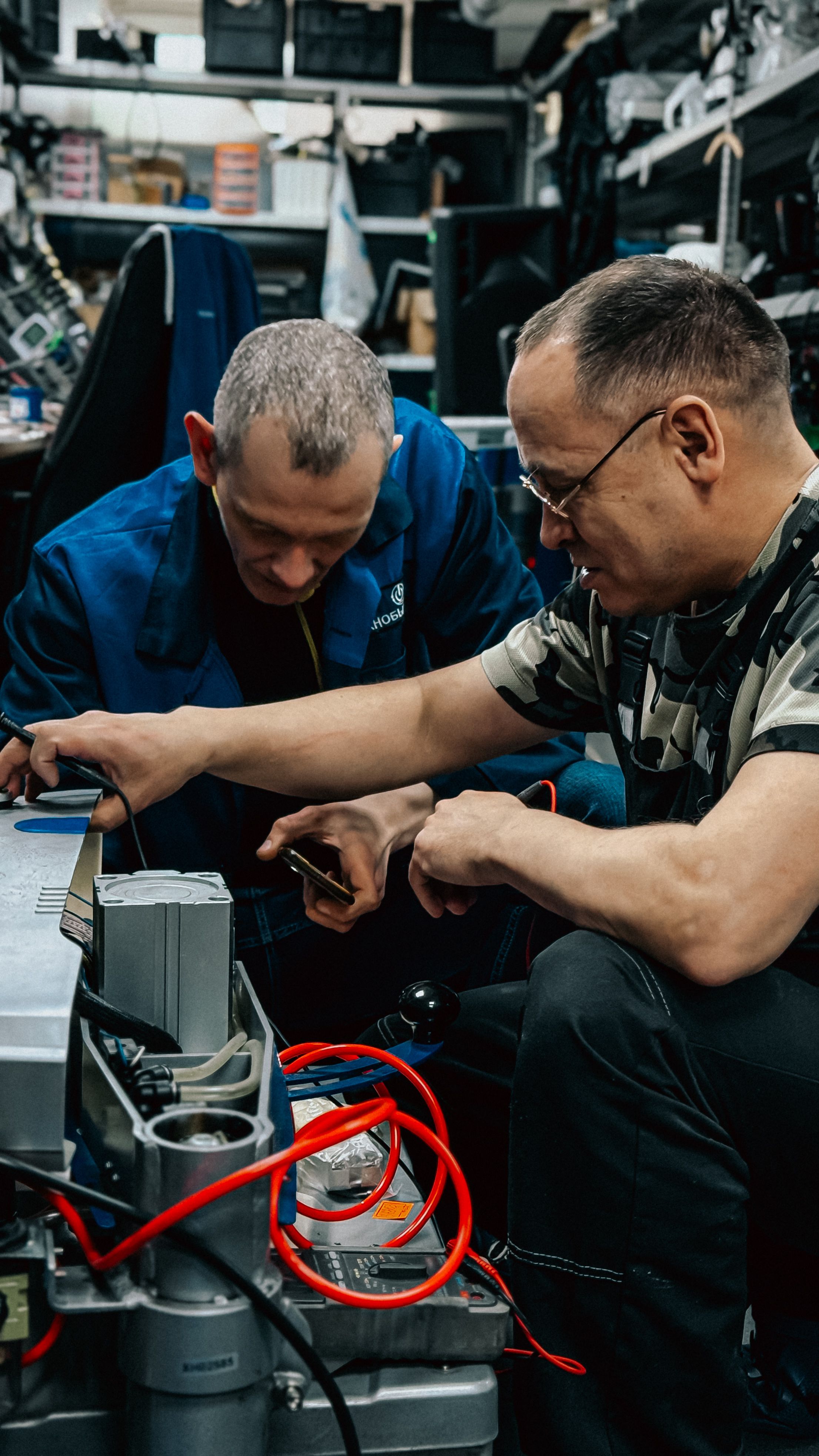 Two adults collaborating on a repair project in a busy workshop environment.