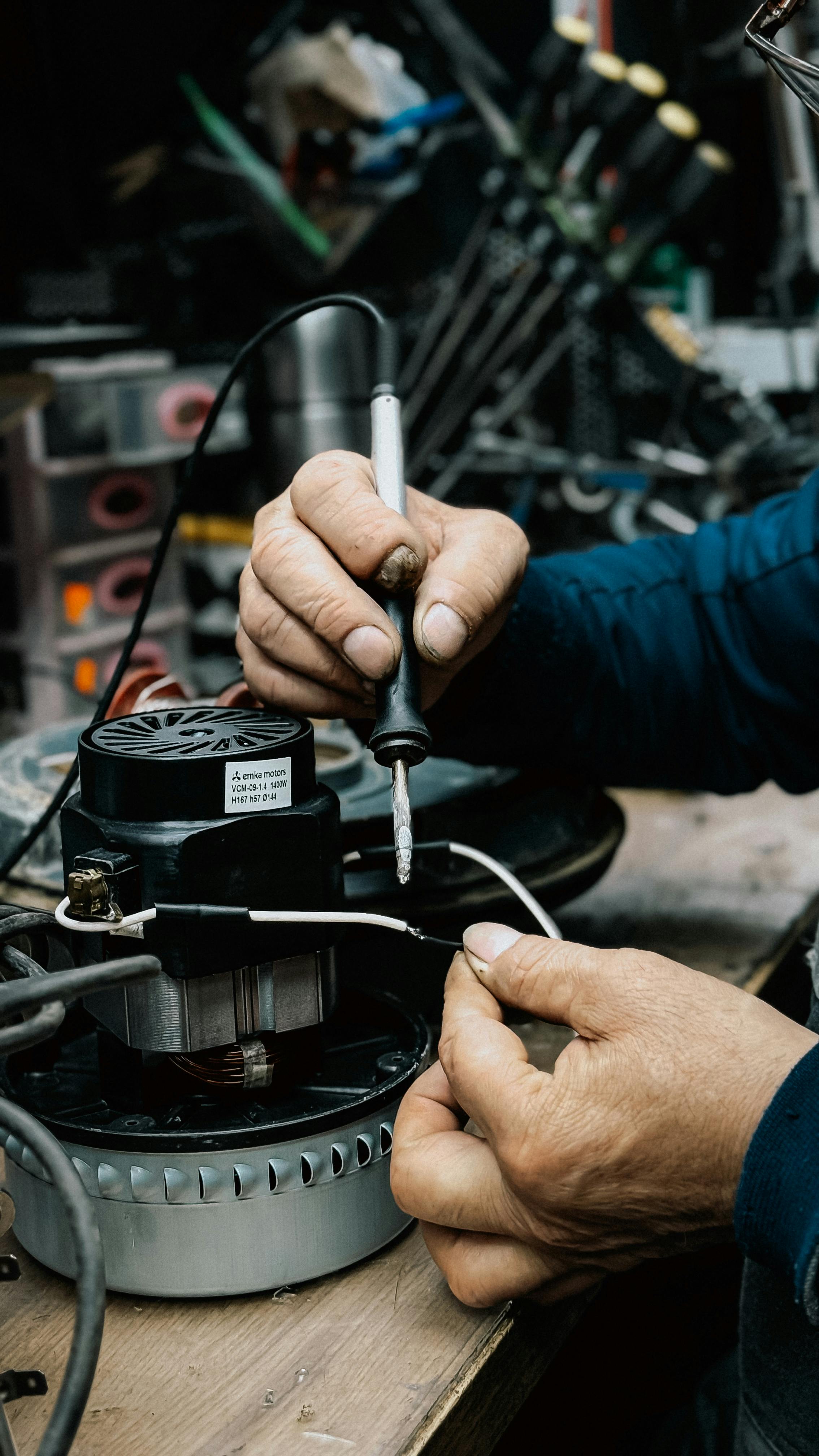 A person skillfully soldering components in a workshop filled with tools and equipment.