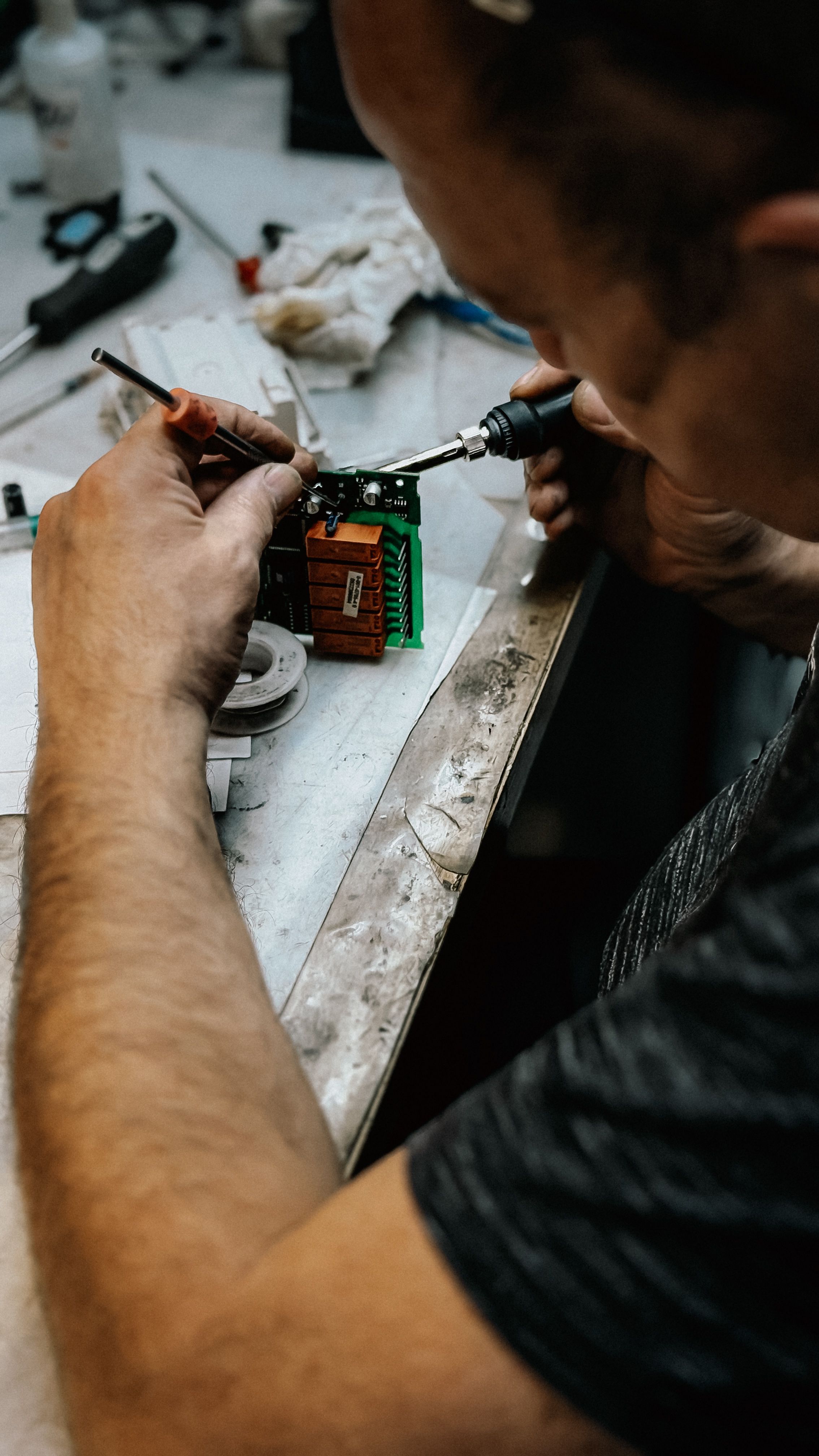 Technician skillfully soldering electronics at a workbench. Close-up details of repair process.