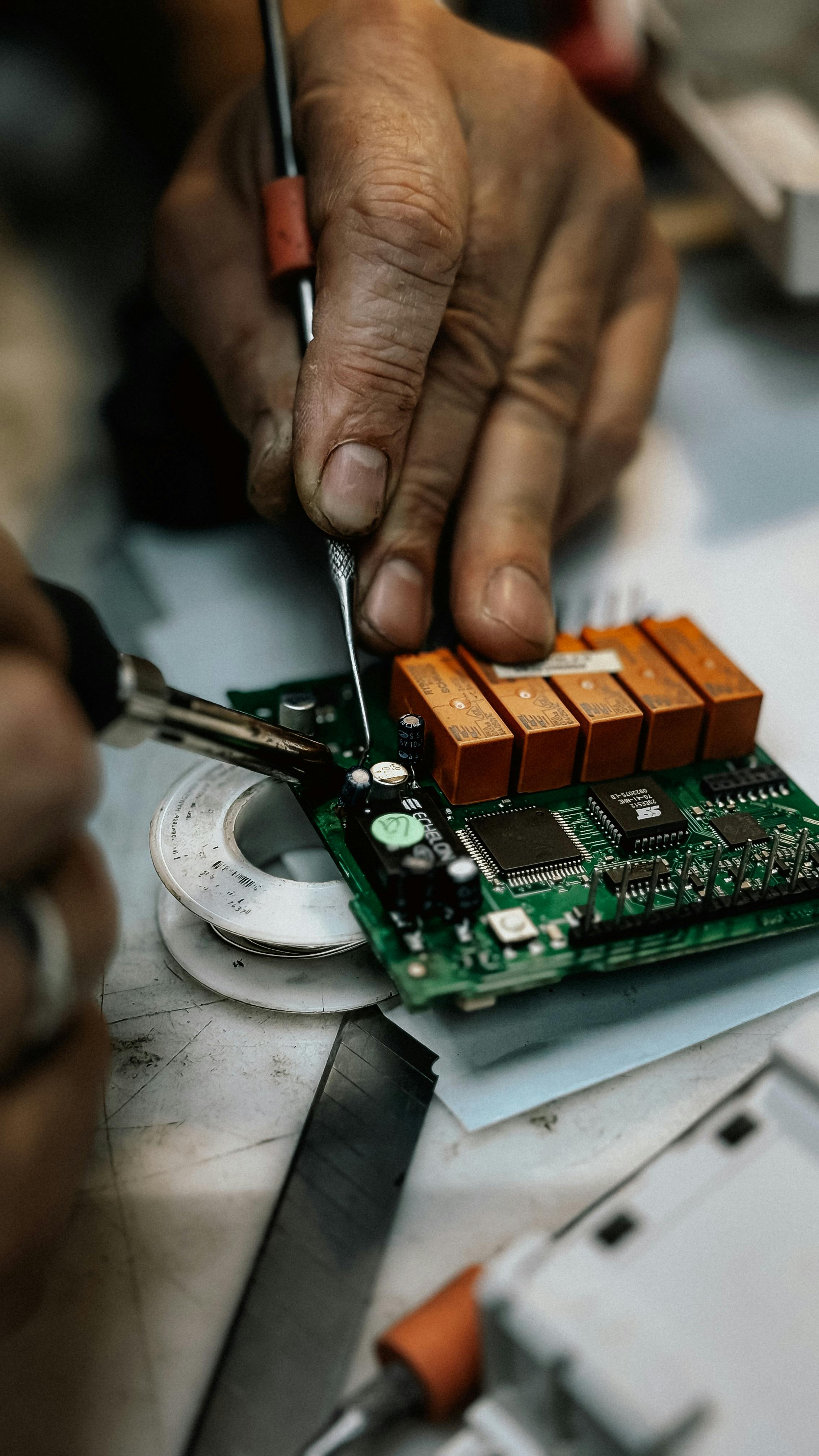 Detailed image of hands soldering and repairing an electronic circuit board.