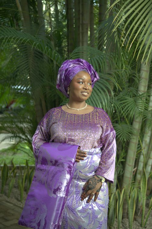 Free Smiling woman in stunning purple traditional Nigerian dress with lush greenery background. Stock Photo