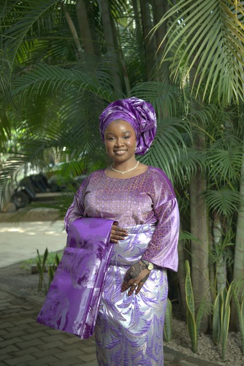 Free Woman in purple Nigerian attire standing outdoors among lush greenery, showcasing elegant cultural fashion. Stock Photo