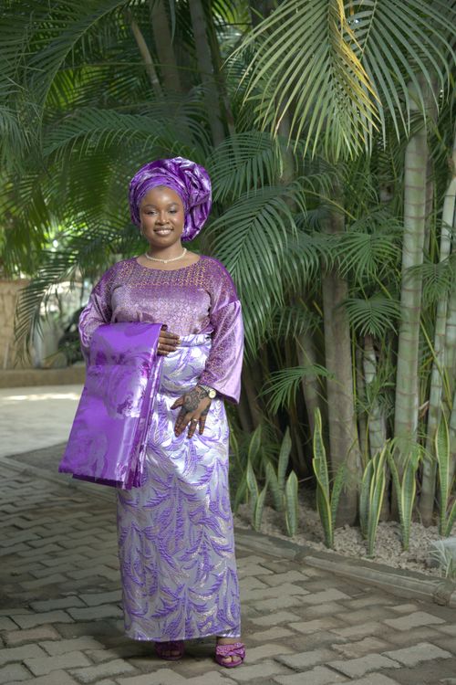 Free A smiling woman in vibrant traditional Nigerian dress stands outdoors among lush greenery. Stock Photo