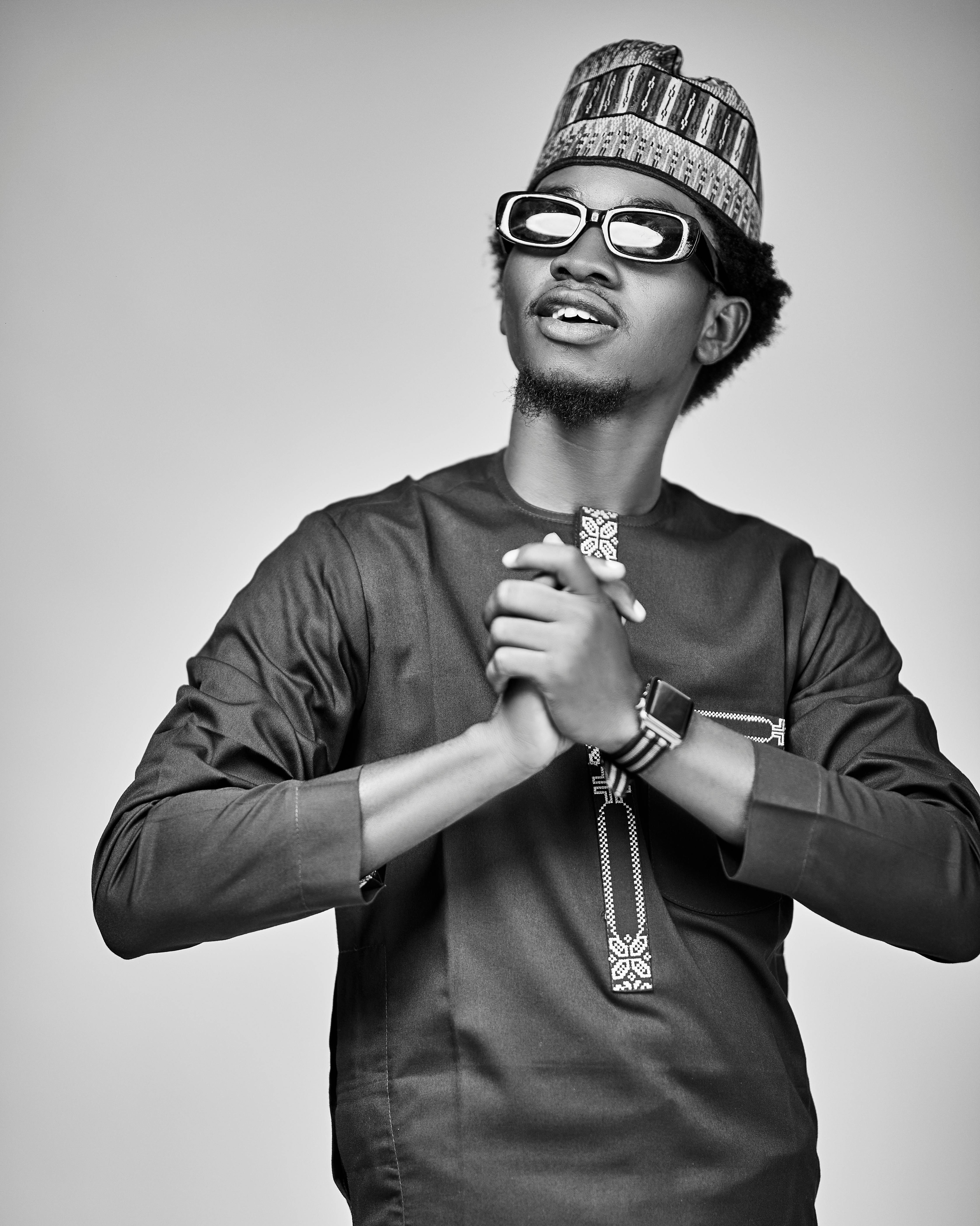 Black and white portrait of a man in traditional Nigerian attire, wearing sunglasses.