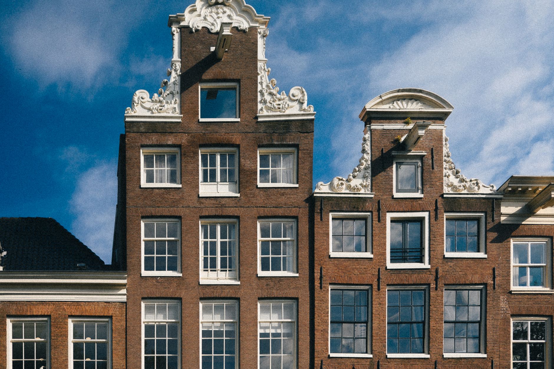 Traditional gabled houses with ornate facades against a blue sky in Amsterdam.
