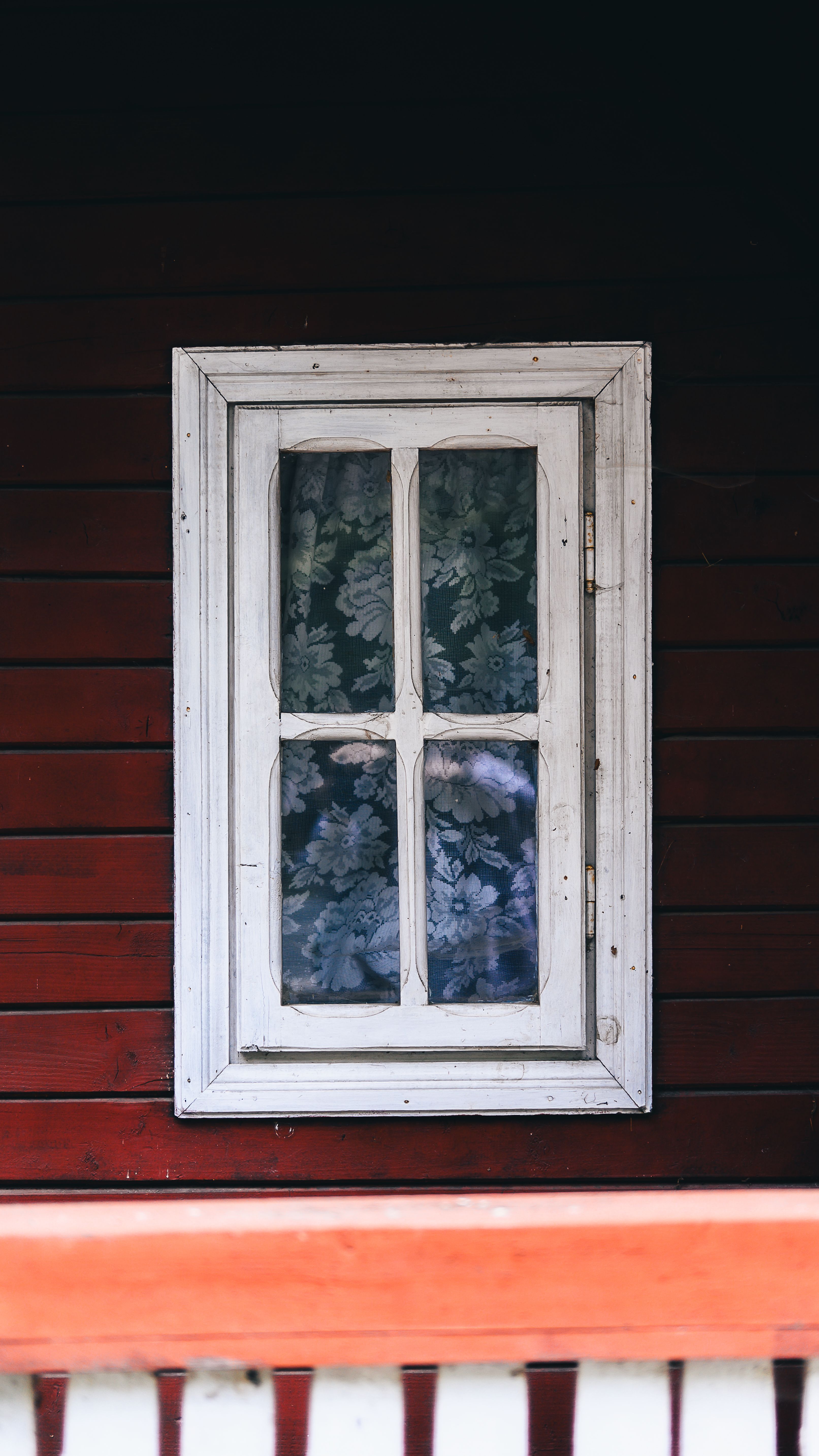 Free A classic white wooden window on a rustic red wooden wall with floral curtains. Stock Photo