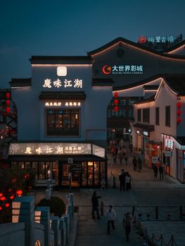 A bustling Chinese street with lit-up signs and traditional architecture at night.