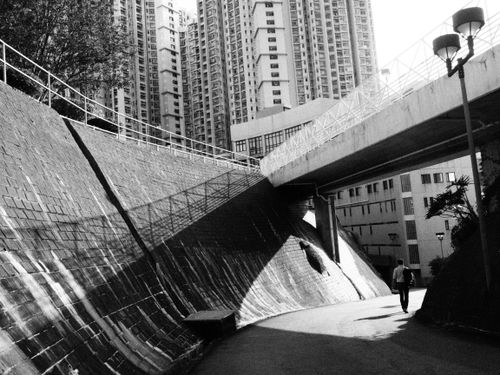 Free Black and white photo of Hong Kong cityscape with a lone walker beneath towering buildings. Stock Photo