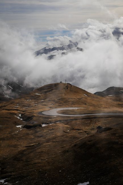 A winding road through a dramatic mountain landscape under a cloudy sky.
