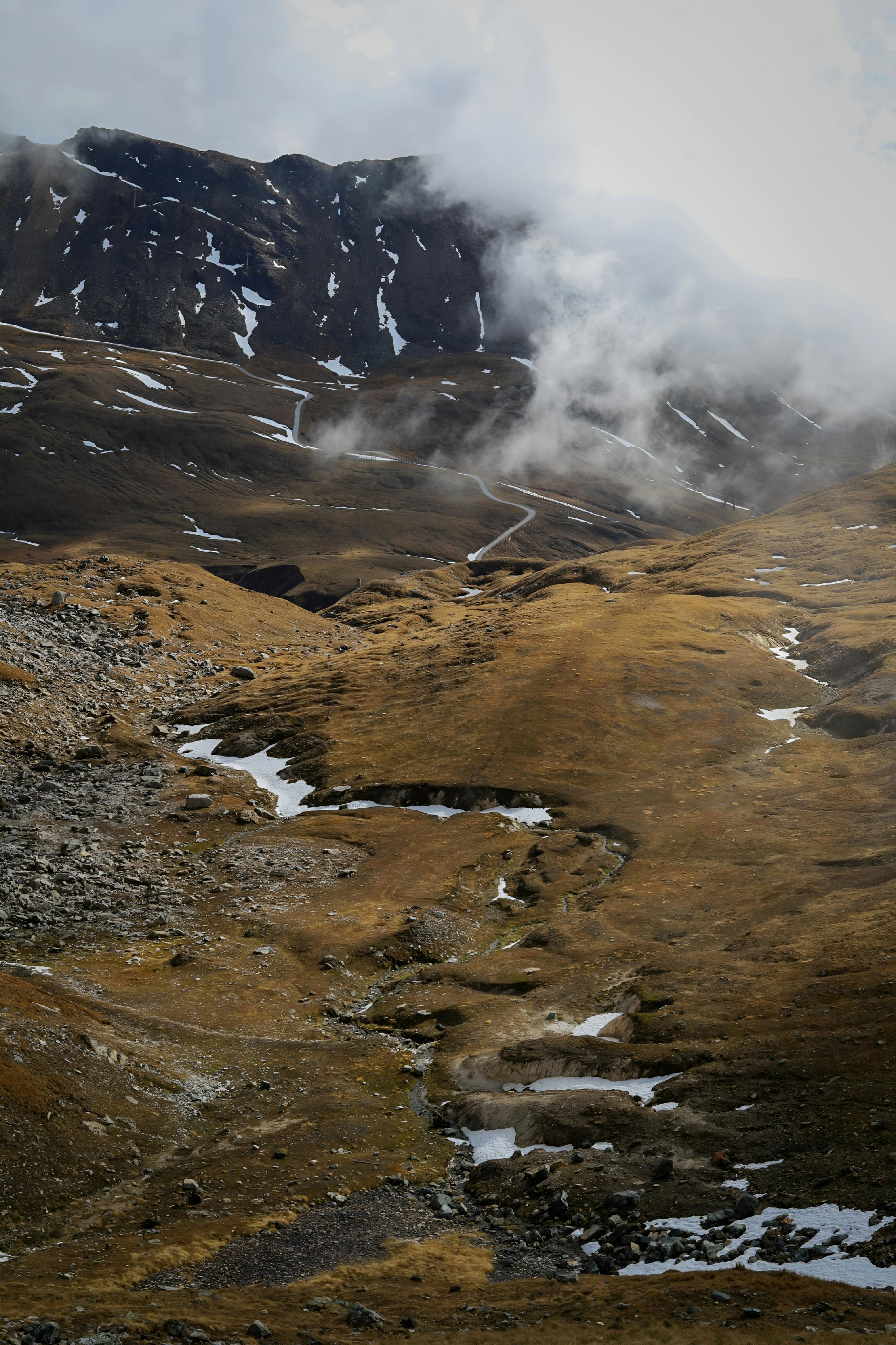 Scenic view of a misty mountain landscape with patches of snow on rugged terrain.