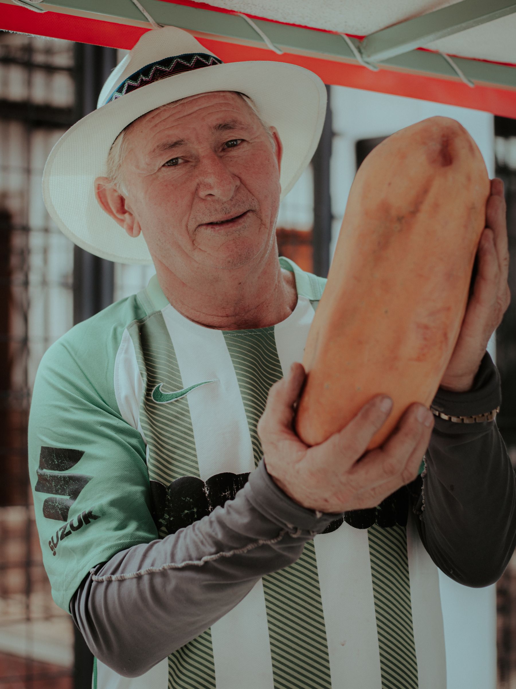 An elderly man proudly holds a papaya at a market in Sabaneta, Antioquia, showcasing Colombian culture.