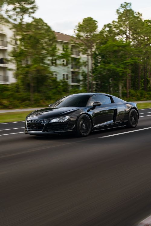 Free Black sports car speeding down road surrounded by lush greenery. Stock Photo