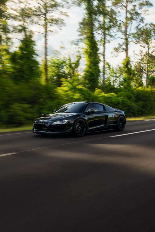 Free A black sports car in motion on a forest-lined road, depicting speed and luxury. Stock Photo