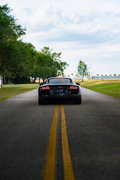Free A sleek black Audi on a quiet, tree-lined open road during the day. Stock Photo