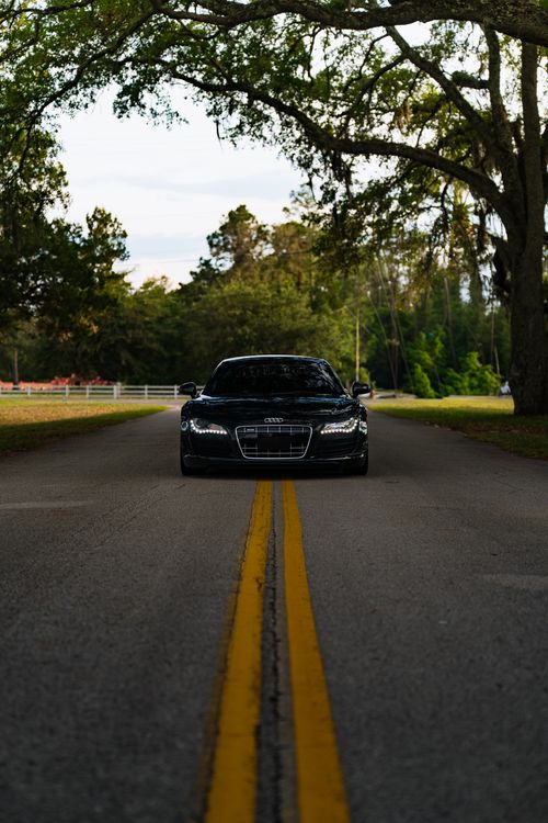 Free Sleek black luxury car driving on a tree-lined rural road, perfect for travel and adventure themes. Stock Photo