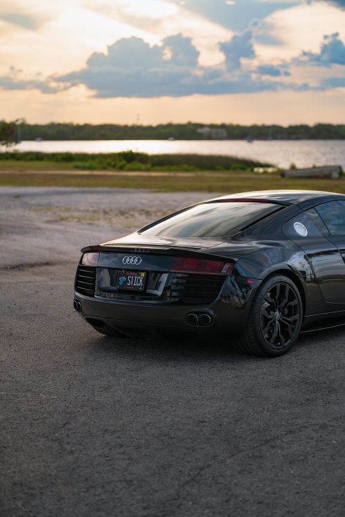 Free A sleek black Audi sports car parked beside a tranquil lake during sunset, exuding luxury and elegance. Stock Photo