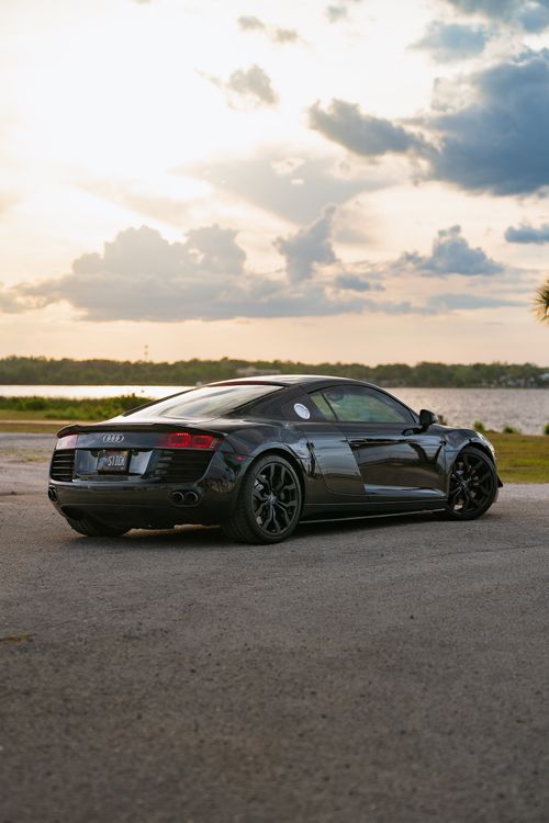 Free A sleek black sports car parked beside a tranquil lake at sunset, capturing elegance and luxury. Stock Photo