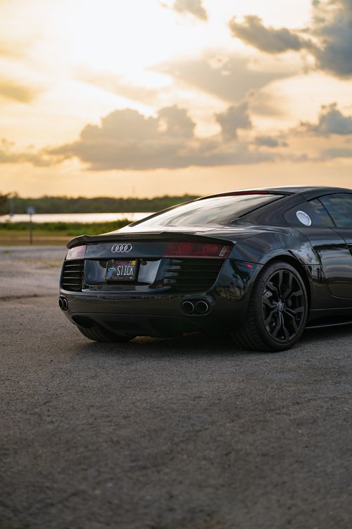 Free Black luxury sports car parked by the lake during a beautiful sunset, showcasing elegance and style. Stock Photo