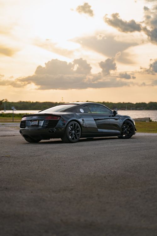 Free A stylish black sports car parked near a calm lake during a picturesque sunset. Perfect for automotive enthusiasts. Stock Photo