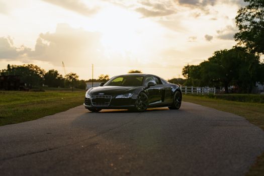A black sports car parked on a quiet road during a golden sunset, evoking a sense of freedom and luxury.