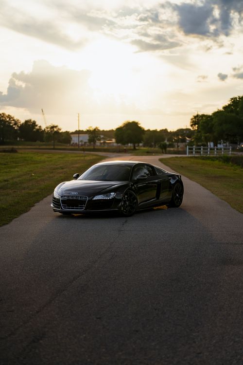 Free High-performance black sports car on a rural road during sunset, showcasing luxury and speed. Stock Photo