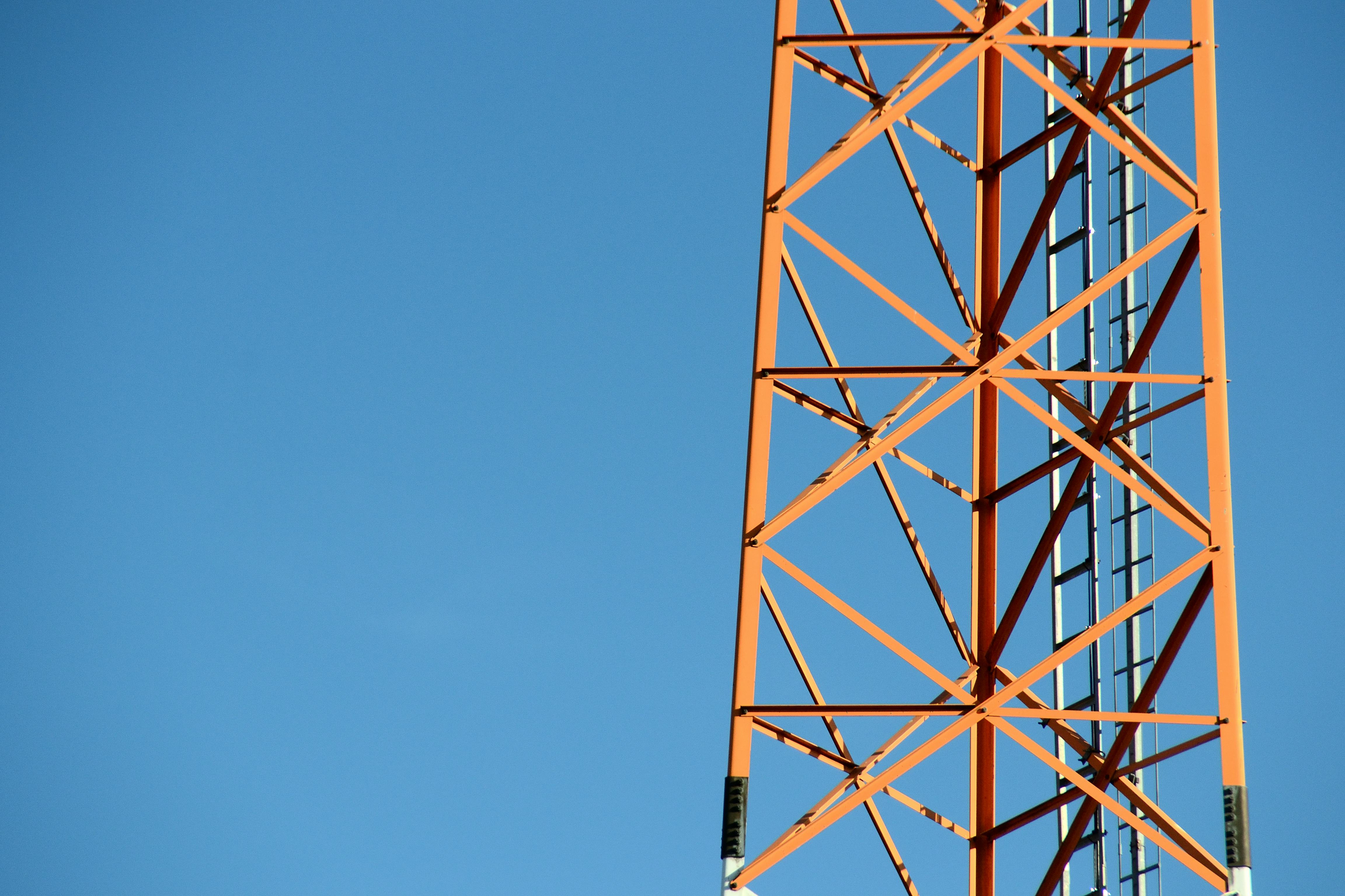Minimalist photo of an orange steel tower against a clear blue sky, showcasing geometric patterns and contrast.