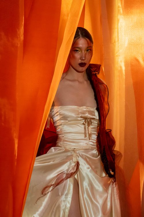Free Striking portrait of a woman in an elegant dress surrounded by vibrant orange fabrics. Stock Photo