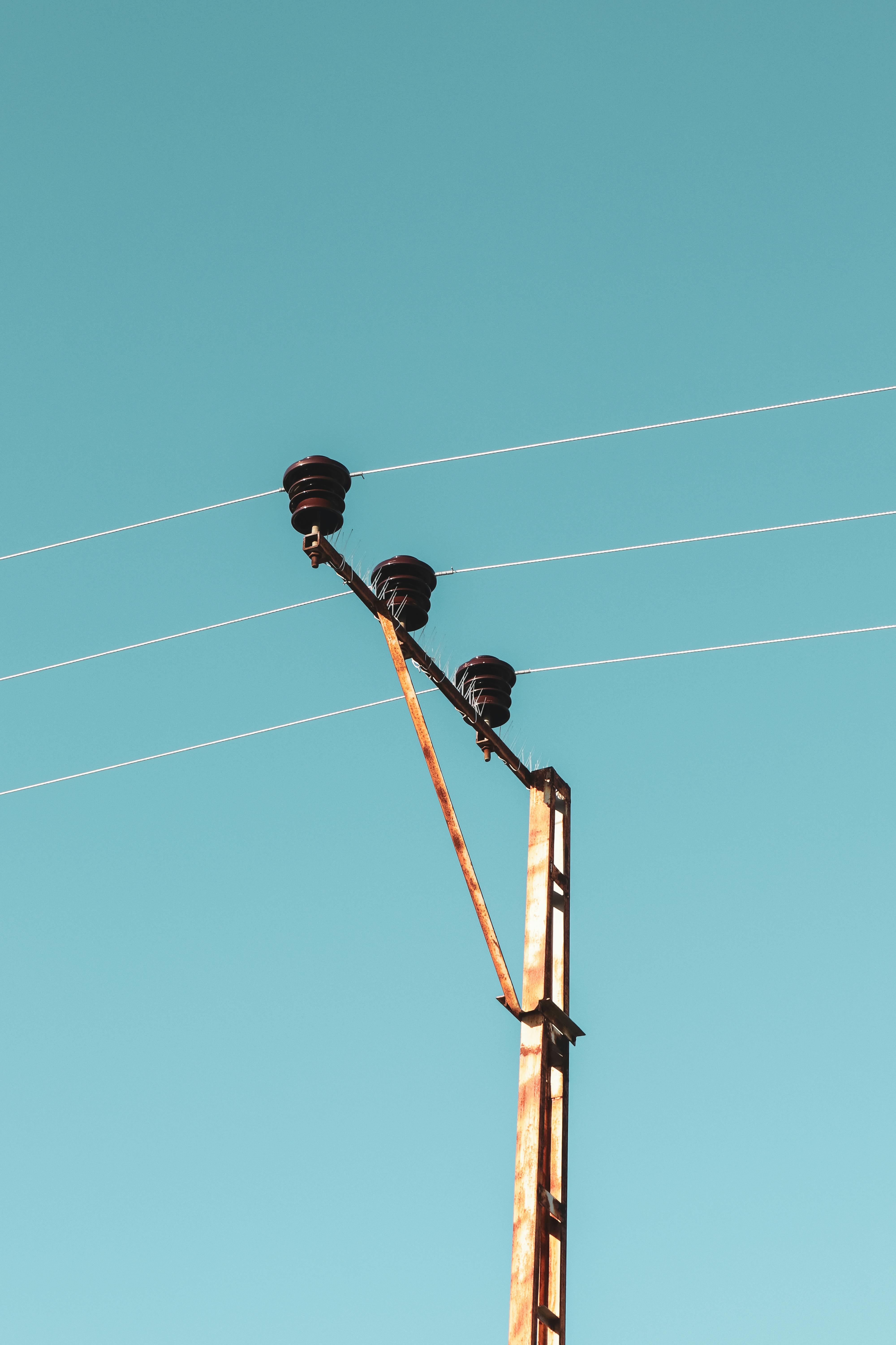 A rustic power line with insulators reaches into a clear sky, symbolizing connection and energy in Battalgazi, Türkiye.
