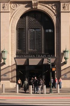 People entering Moynihan Train Hall on a sunny day, showcasing detailed architectural design.