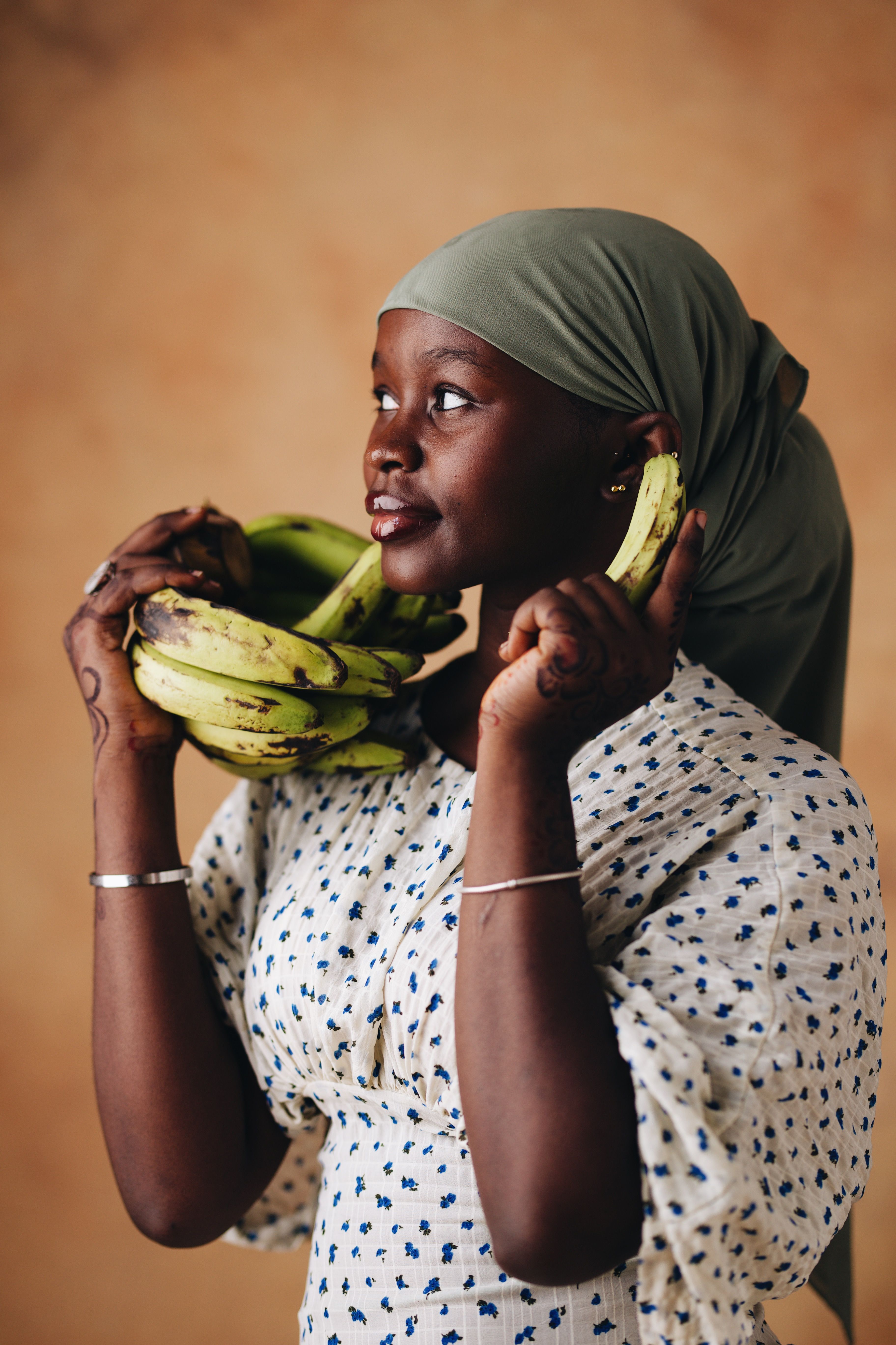 Smiling woman with green headscarf holding bananas, expressing joy and contentment.
