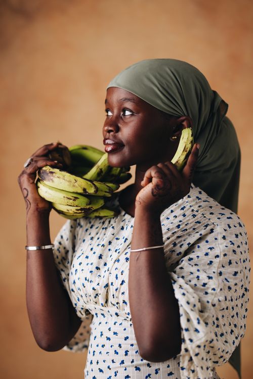 Free Smiling woman with green headscarf holding bananas, expressing joy and contentment. Stock Photo