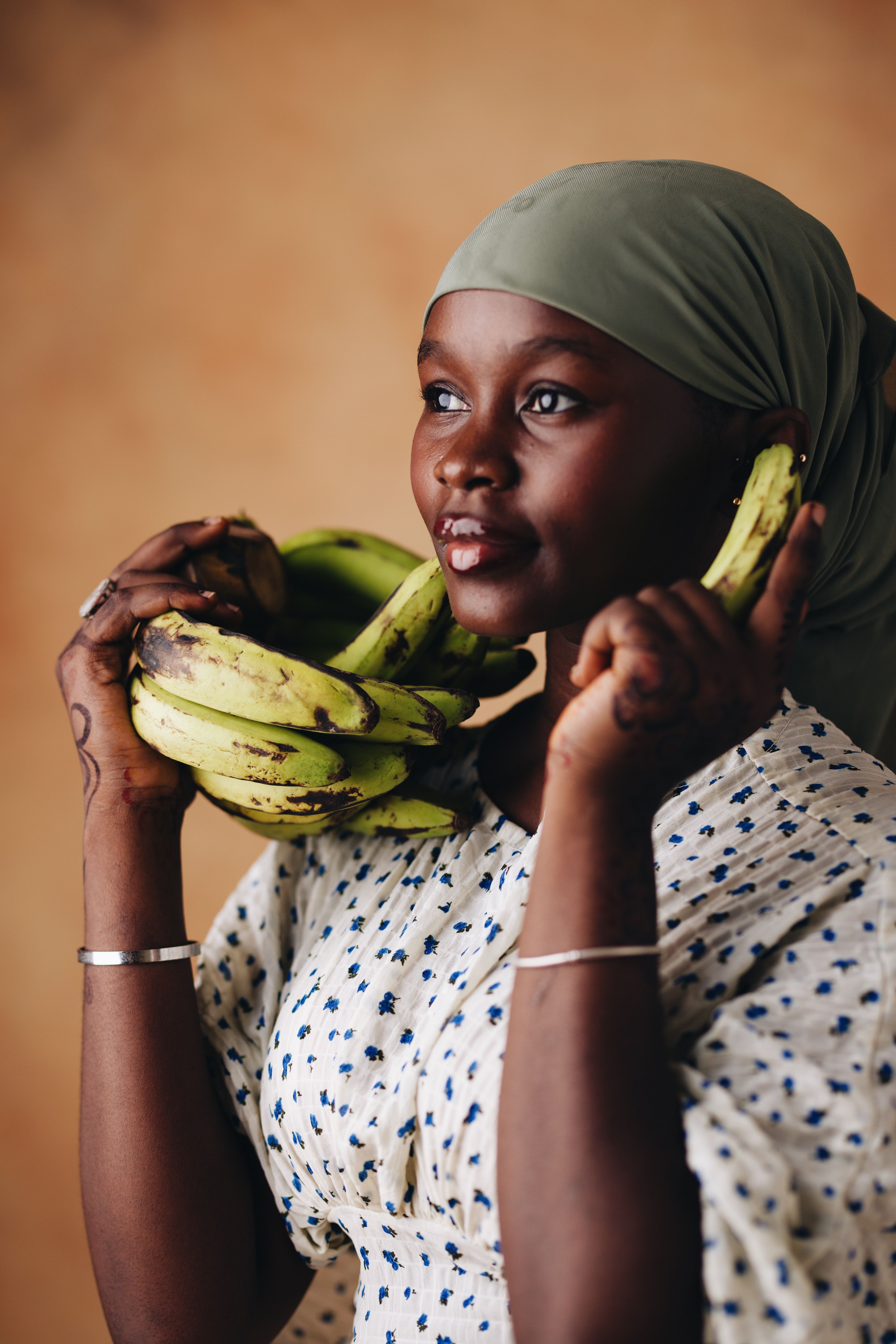 A woman in a headscarf gracefully holds fresh green bananas, capturing a moment of cultural elegance.