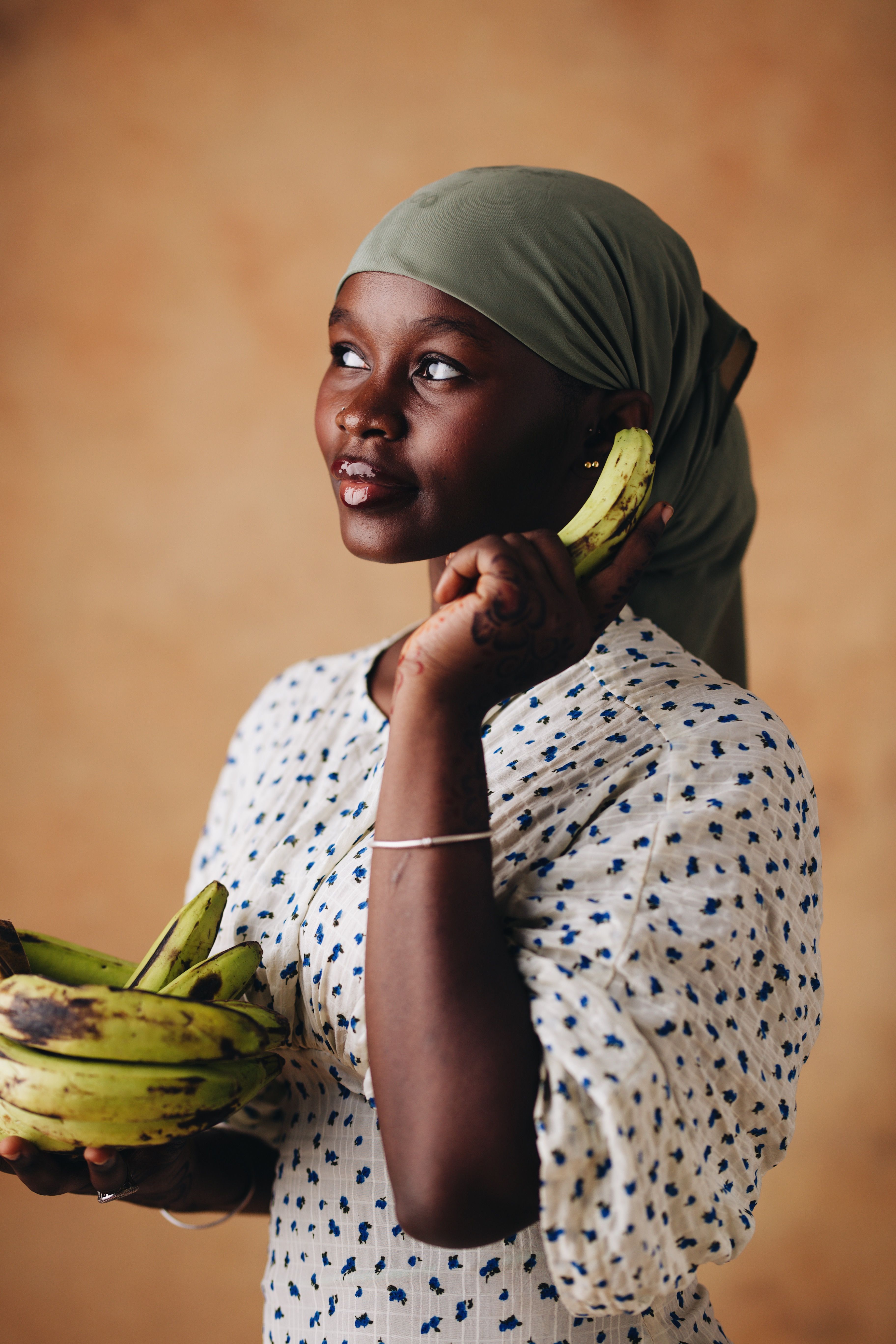 A woman in traditional attire thoughtfully holds bananas against a neutral background.