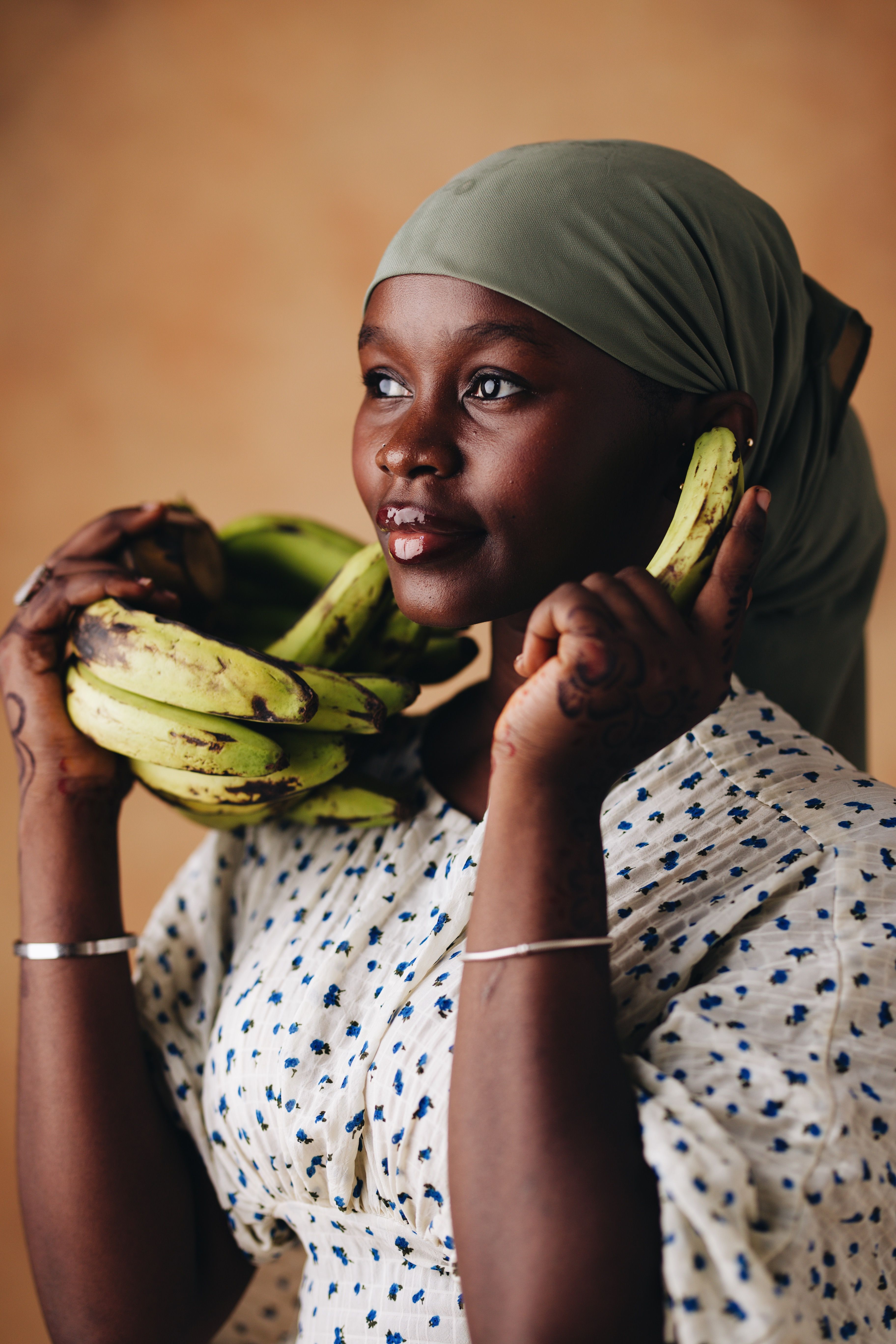 Portrait of a smiling woman in a headscarf holding bananas indoors.