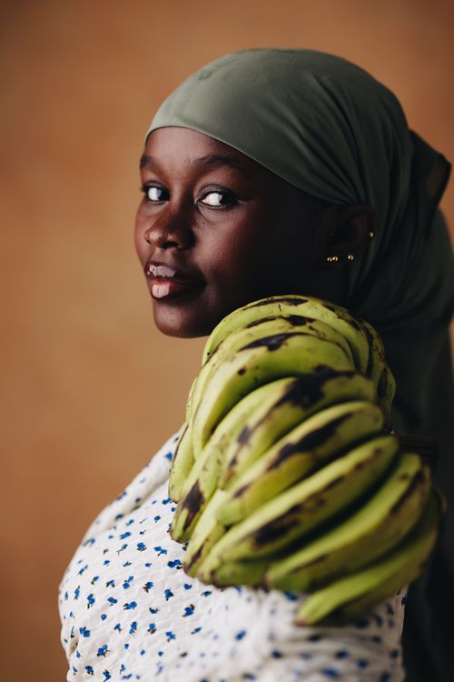 Free Smiling woman with green plantains on her shoulder, wearing a headscarf. Stock Photo