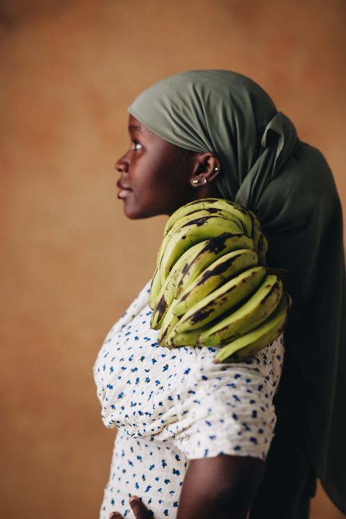 Free Profile of a woman in a headscarf carrying green bananas, showcasing daily life and tradition. Stock Photo