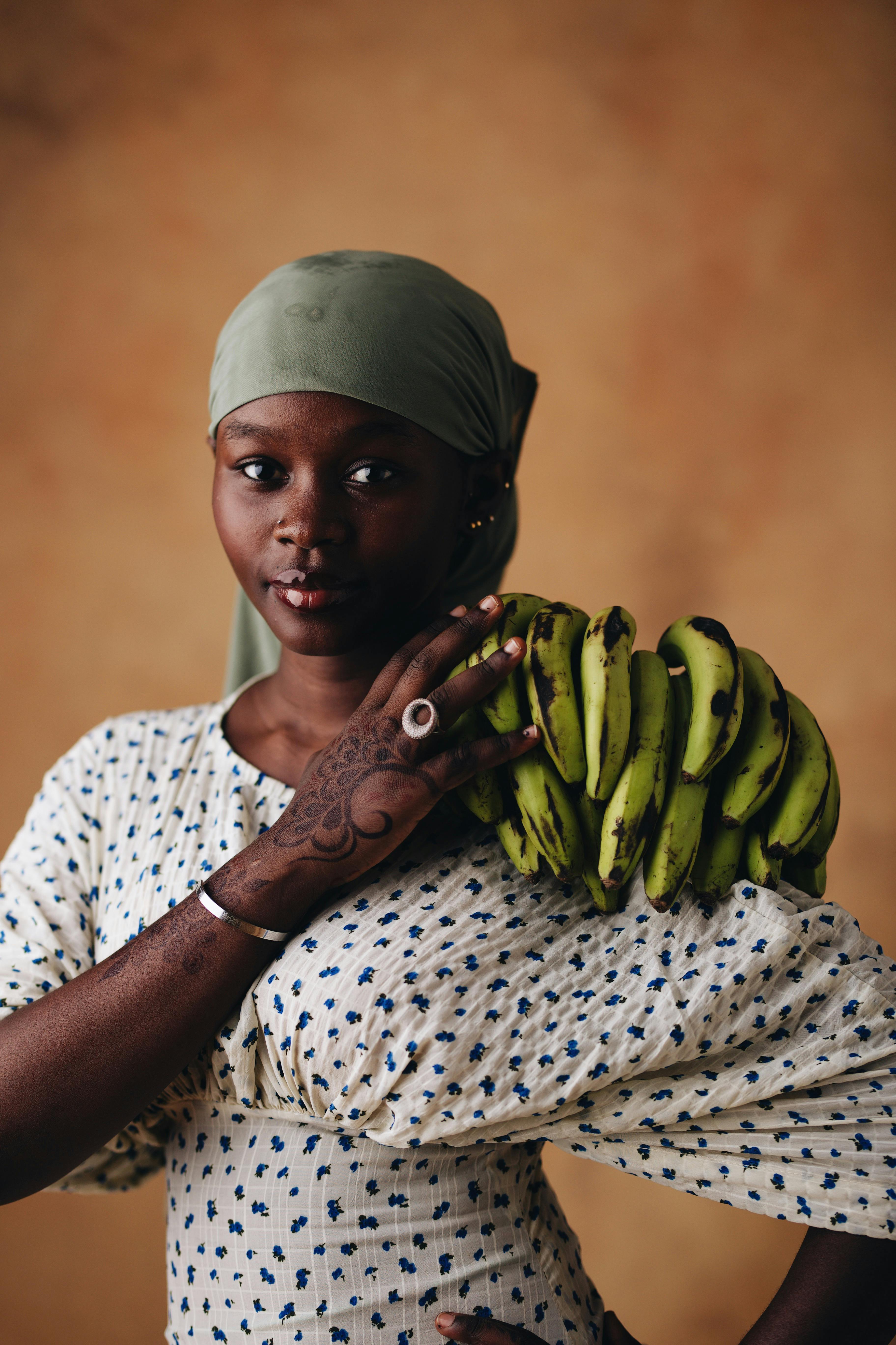 Cultural portrait of a woman carrying green bananas, showcasing traditional attire and intricate henna design.