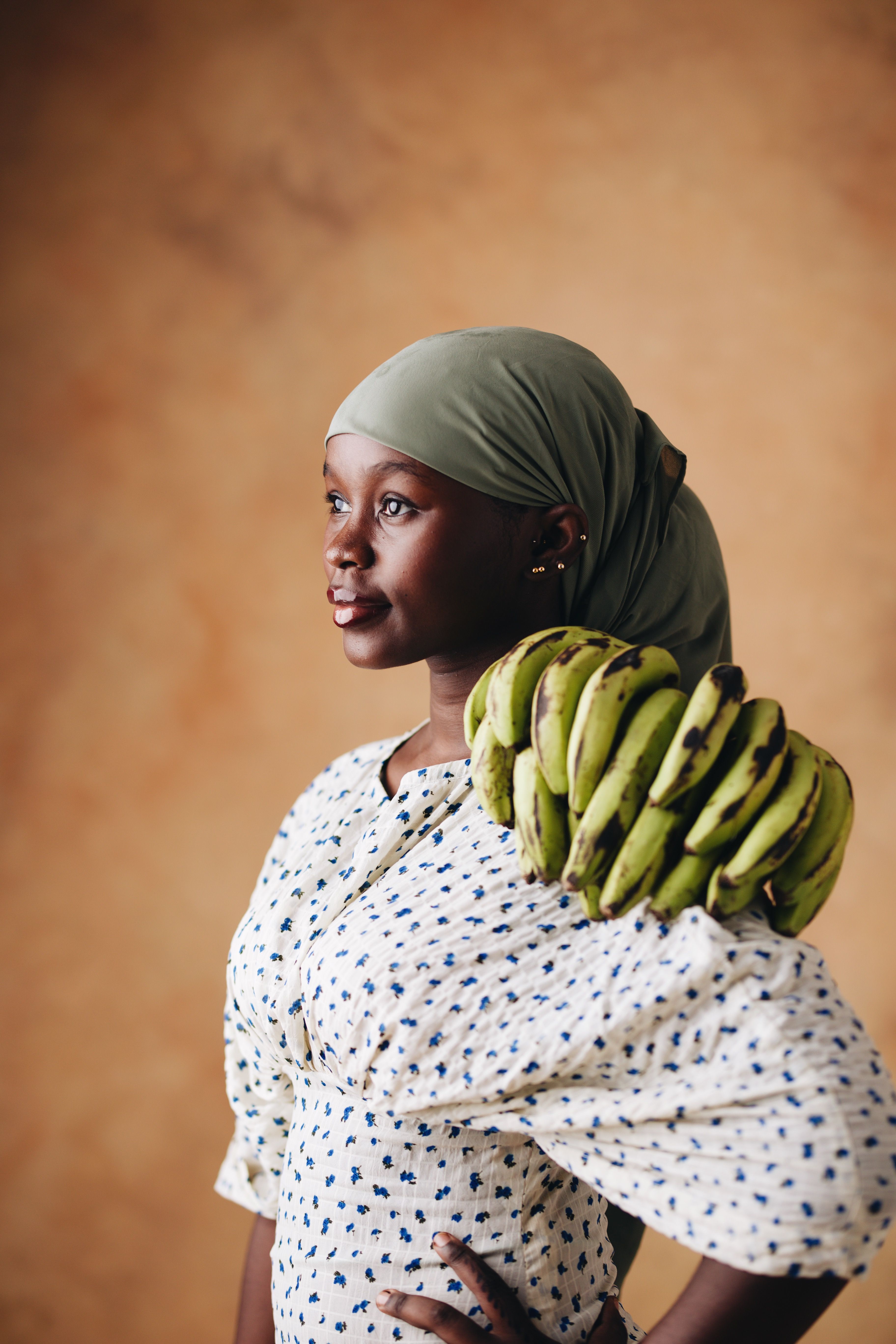 A woman in traditional attire carries fresh bananas against a warm backdrop.
