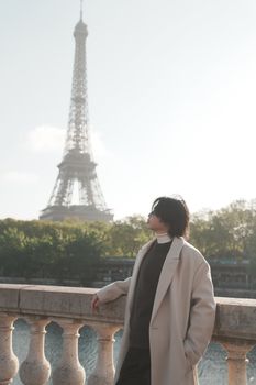 Person in fashionable coat standing by the Eiffel Tower on a clear day in Paris.