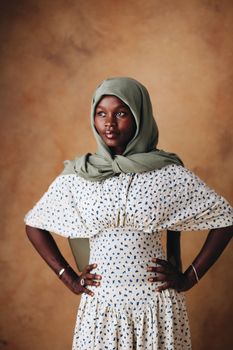 Portrait of a woman wearing a stylish patterned dress with a green hijab against a warm background.
