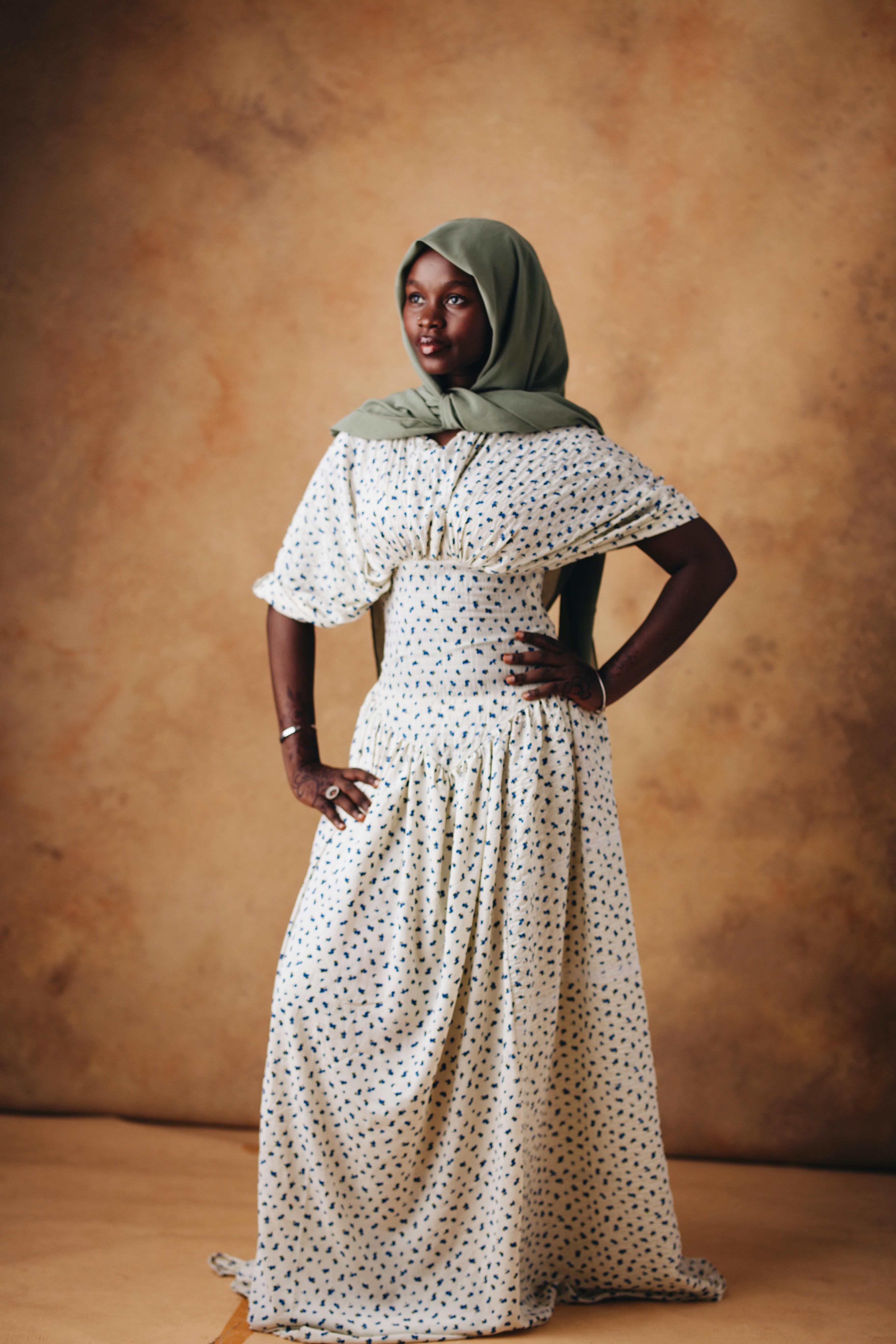 Stylish woman in a long polka dot dress with a headscarf, posing confidently indoors.