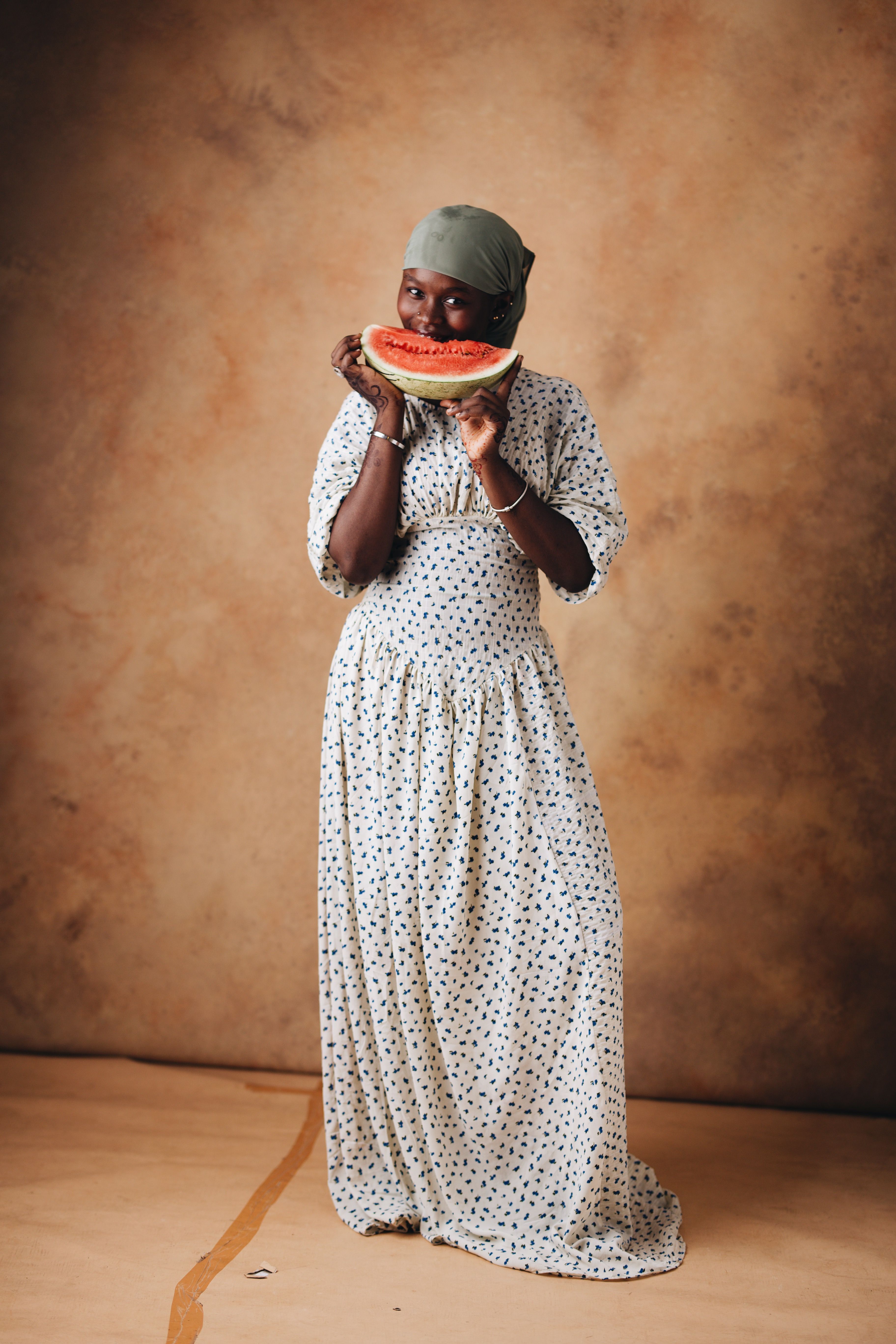 Smiling woman in a polka dot dress indoors holding a slice of watermelon.